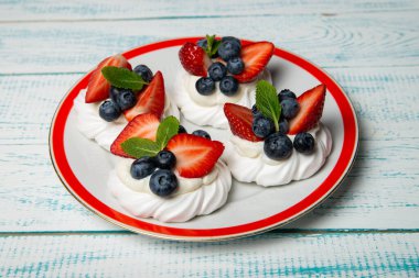 Dört pasta Anna Pavlova ile yaban mersini ve güzel bir tabakta nane yaprağı ile çilek. Ev yapımı şekerleme. Eski beyaz ve mavi masa.