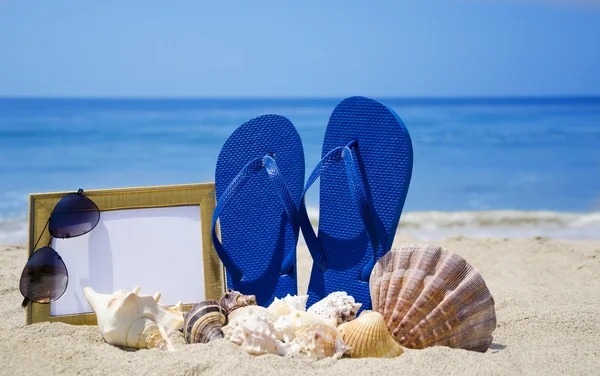 Chanclas con marco fotográfico y conchas marinas en la playa de arena —  Fotos de Stock