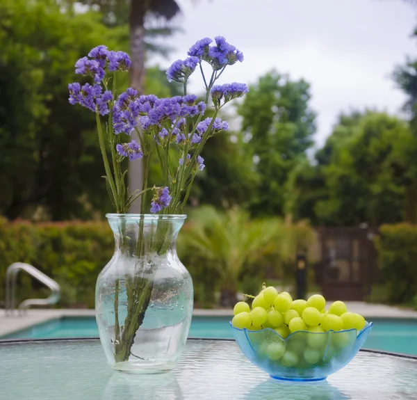Vase with flowers and grapes by the pool — Stock Photo, Image