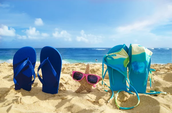 Flip flops, bikini and starfish with sunglasses on sandy beach — Stock Photo, Image