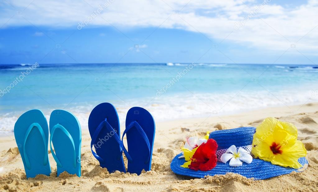 Flip flops and hat with tropical flowers on sandy beach