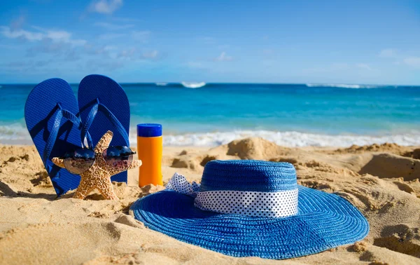 Flip flops, sunscreen, hat and starfish on sandy beach — Stock Photo, Image