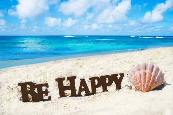 Firma "Sé feliz" y concha marina en la playa de arena — Foto de Stock