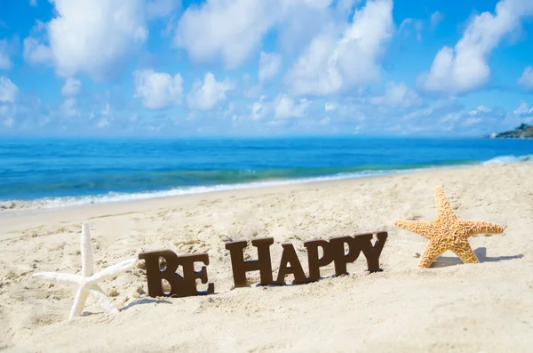 Sign "Be Happy" and two starfish on the sandy beach — стоковое фото