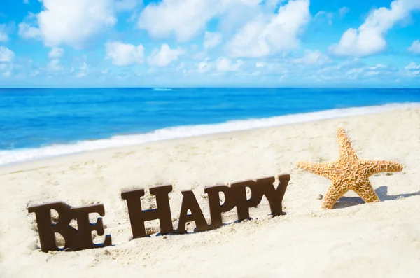 Firma "Sé feliz" y las estrellas de mar en la playa de arena — Foto de Stock