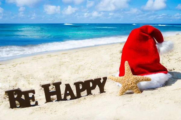 Assine "Seja feliz" e estrela do mar com chapéu de Natal na bea arenosa — Fotografia de Stock