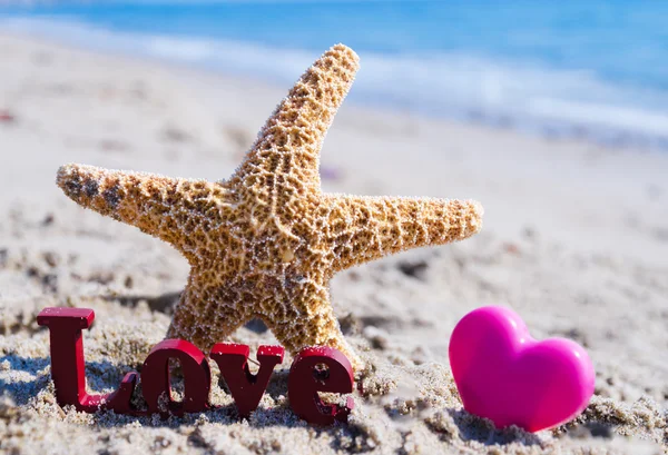 Sign "LOVE" with starfish and heart on the beach — Stock Photo, Image