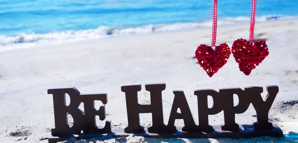 Знак "Бути щасливим" з серцями на пляжі — стокове фото