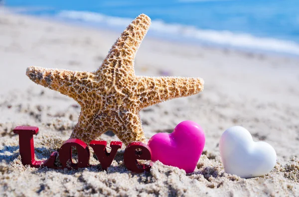 Assine "AMOR" com estrelas do mar e corações na praia — Fotografia de Stock