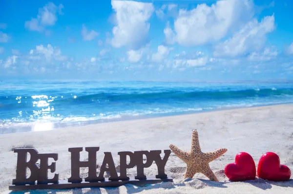 Tanda "Berbahagialah" dengan bintang laut dan hati di pantai — Stok Foto