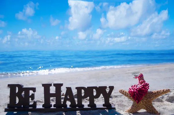 Assine "Seja feliz" com estrelas do mar e coração na praia — Fotografia de Stock