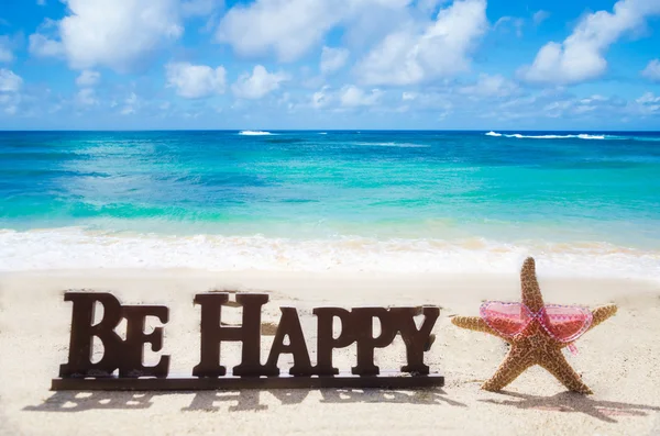 Registrera "vara lycklig" på sandstranden med sjöstjärna — Stockfoto