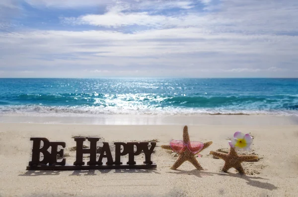 Schild "Sei glücklich" am Sandstrand mit Seesternen — Stockfoto