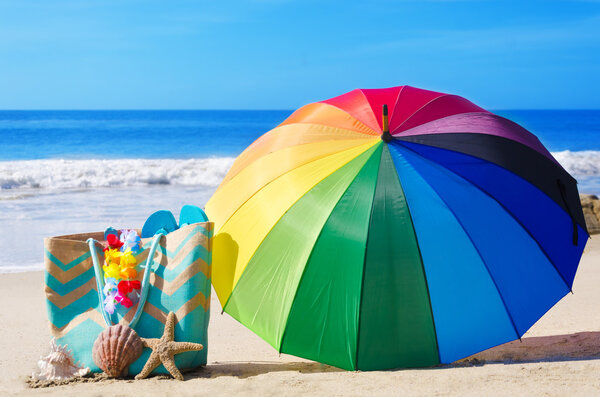 Summer background with rainbow umbrella and beach bag