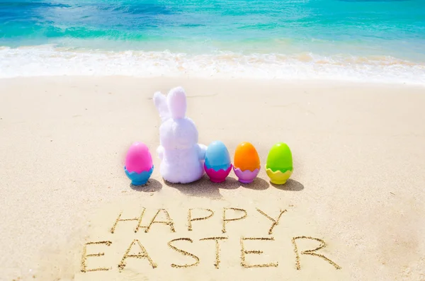 Assine "Feliz Páscoa" com coelhinho e ovos coloridos na praia — Fotografia de Stock