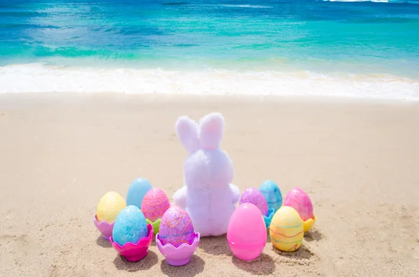 Velikonoční zajíček a barevná vajíčka na pláži — Stock fotografie