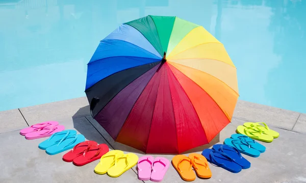 Color umbrella and flip flops by the pool — Stock Photo, Image