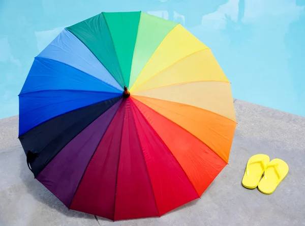 Guarda-chuva de cores e chinelos à beira da piscina — Fotografia de Stock