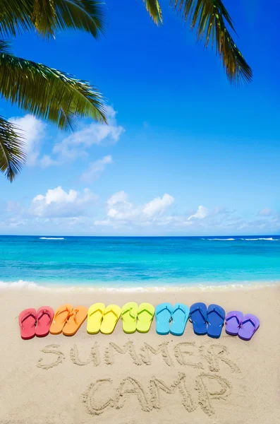 Sign "Summer camp" and color flip flops on sandy beach — Stock Photo, Image