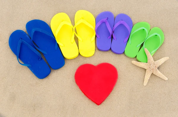 Färg flip flops och hjärtat på sandstrand — Stockfoto