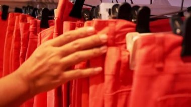 Kadın eli, elbise mağazasında askıda turuncu kot pantolon boyunda seçiyor..