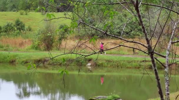 田径上的女运动员在池塘边的小径上跑步健身 女赛跑选手早上在大自然中奔跑 健康生活方式的概念 — 图库视频影像