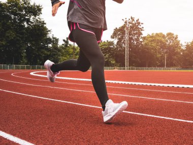 Stadyum pistinde spor kıyafetleriyle koşan atletik bir kadın. Kadın koşucu egzersiz için koşuyor. Spor Sağlıklı yaşam tarzı konsepti.