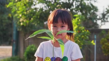 Asyalı küçük kız baharda açık havada genç bitkileri tutuyor. Çevre ve dünyayı kurtarma kavramı.