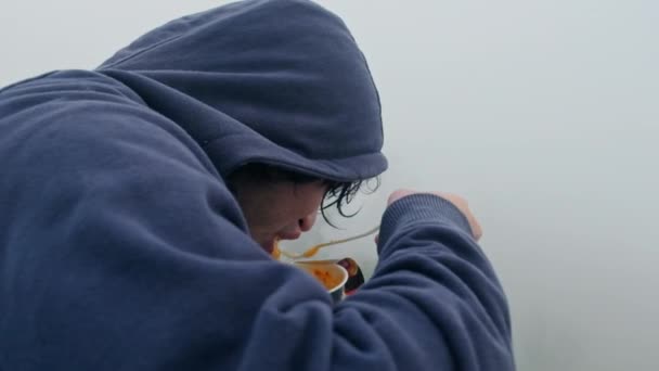 年轻男子身穿海军蓝男帽运动衫 长袖长袖 吃方便面 欣赏山水 背阴浓雾 — 图库视频影像