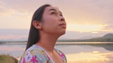 Gölün kenarında duran genç bayan turist gün batımında doğanın güzel manzarasının tadını çıkarıyor. Yaşam tarzı ve açık hava turizm kavramları.