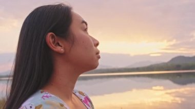 Gölün kenarında duran genç bayan turist gün batımında doğanın güzel manzarasının tadını çıkarıyor. Yaşam tarzı ve açık hava turizm kavramları.