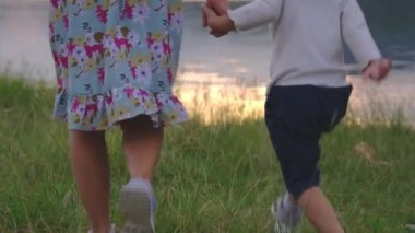 Mutlu anne ve çocuklar bir yaz günü gün batımında göl kenarında el ele yürürler. Mutlu aile tatilde birlikte vakit geçirir..