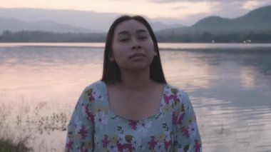 Genç Asyalı bir kadının portresi göl kenarında gün batımında temiz hava soluyor..