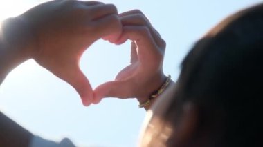 Hand of happy little girl at sunset. Happy little girl's hand reached out and made a heart shape to the sun silhouette sunlight. Heart symbol of family love.