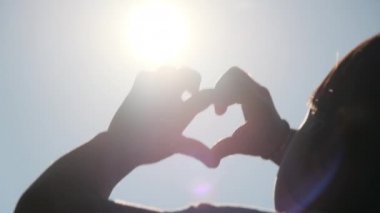 Gün batımında küçük mutlu bir kızın eli. Mutlu küçük kızın eli uzandı ve güneş siluetine kalp şeklinde bir ışık yaptı. Aile sevgisinin kalp sembolü..
