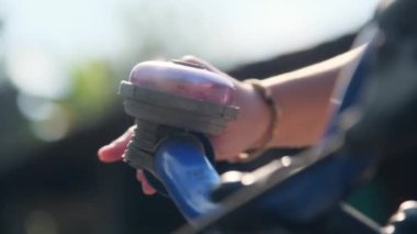 Close-up of a child's hand ringing a bicycle bell on a bicycle handlebar in a park.
