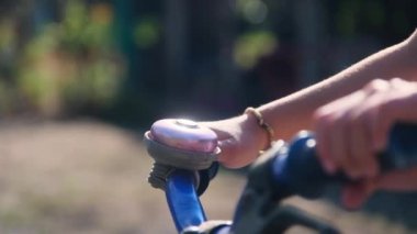 Close-up of a child's hand ringing a bicycle bell on a bicycle handlebar in a park.