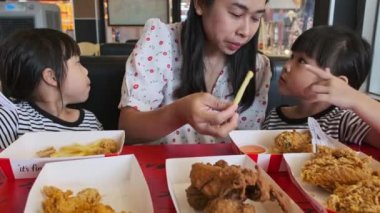 Fast food restoranında güzel bir anneyle birlikte kızarmış tavuk ve patates kızartması yiyen tatlı Asyalı kızlar..