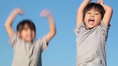Happy sisters raising their hands and jumping in the summer garden at sunset. Cheerful girls jumping and playing in the park.