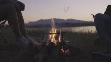 Neşeli genç arkadaşlar gölün kenarında kamp ateşi etrafında otururlar..