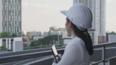 Beyaz şapkalı kendine güvenen bir kadın mimar kameraya gülümseyerek bakıyor. İnşaat alanında tablet bilgisayarı olan kadın inşaat mühendisi..