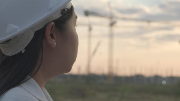 日没時に建設現場にタブレットコンピュータを持つ女性の建設エンジニア 建設現場を見て白いヘルメットに自信のある女性建築家 — ストック動画