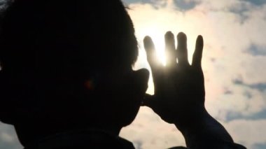 Akşam güneşine uzanan yaşlı bir adamın silueti. Gün batımında mutlu bir kıdemli adamın elleri..