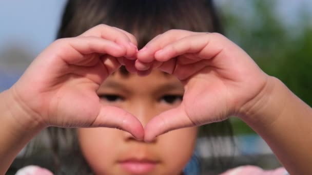 小さなアジアの女の子がカメラを見て 彼女の手で心の形を作ります 愛のハートシンボル — ストック動画