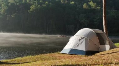 Güneşin doğuşunda sisli nehrin üzerinde, Bambu salındaki gezginin arka planına karşı güzel bir göl kenarında kamp çadırı. Mahremiyet turizmi ve özgürlük kavramı.