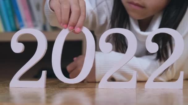 可爱的小女孩把白色的2022号放在一个木制桌子室内 新的一年2022 — 图库视频影像