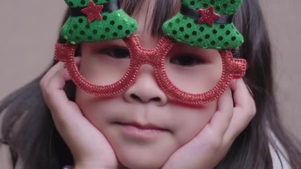 自宅で面白いクリスマスの眼鏡で愛らしい少女の肖像画 メリークリスマスとハッピーニューイヤー — ストック動画