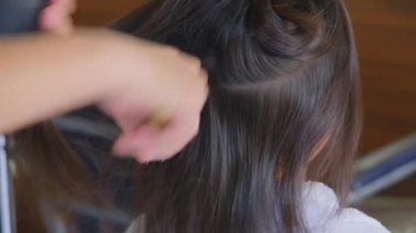 Asyalı küçük kız saçını bir kuaför tarafından bir güzellik salonunda kurutuluyor. Kuaför küçük tatlı kızlar için saç stili yapar..