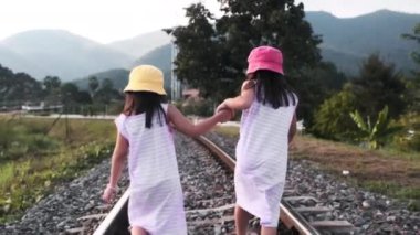 İki tatlı Asyalı kız kırsal bölgedeki tren raylarında akşamları dağlara karşı birlikte koşuyorlar..