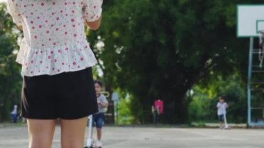 Mutlu anne ve çocuklar yaz parkında scooter sürerken beşlik çakıyorlar. Çocuklar dışarıda scooterlarla oynuyor. Çocuklar için boş zaman aktiviteleri ve açık hava sporları
